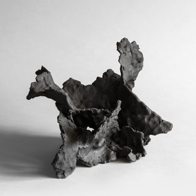 Dark stoneware sculpture with wave-like forms and textured surface, resembling drift or motion.