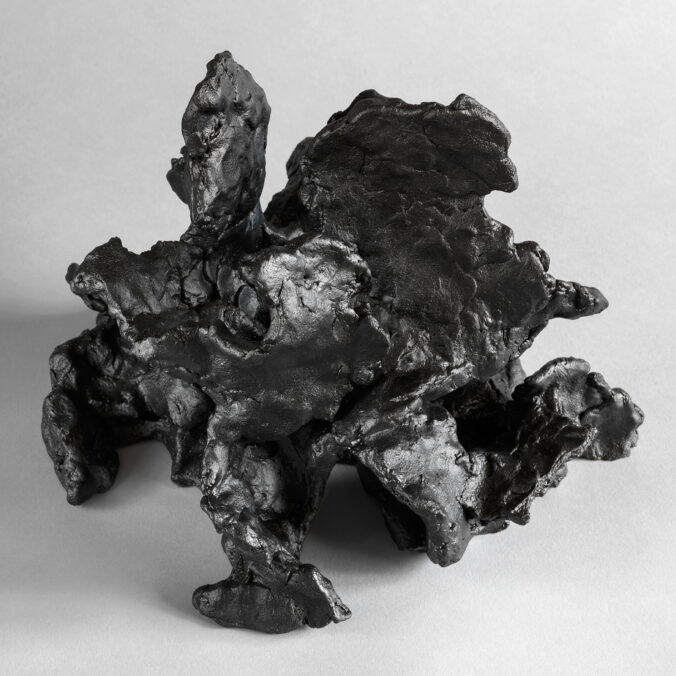 Dark stoneware sculpture with layered, organic textures and a fluid, wave-like composition.
